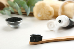 Charcoal toothbrush sitting in foreground with charcoal toothpaste in background